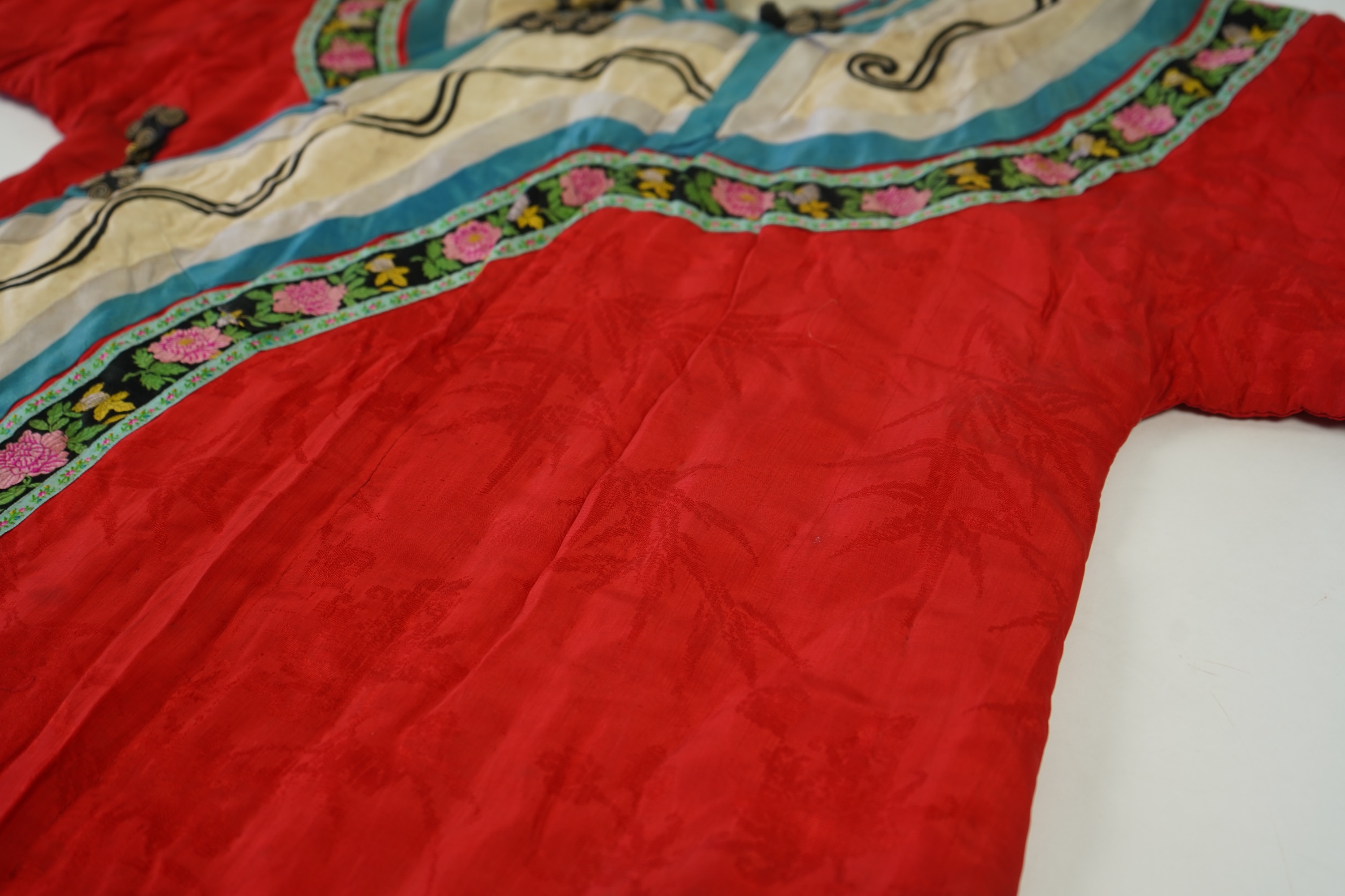 A late 19th century early 20th century Chinese red silk damask quilted Mandarin robe. Decorated with colourful rows braiding and ornate toggling. 116cm long. Condition - minor marks in places, may benefit from specialist